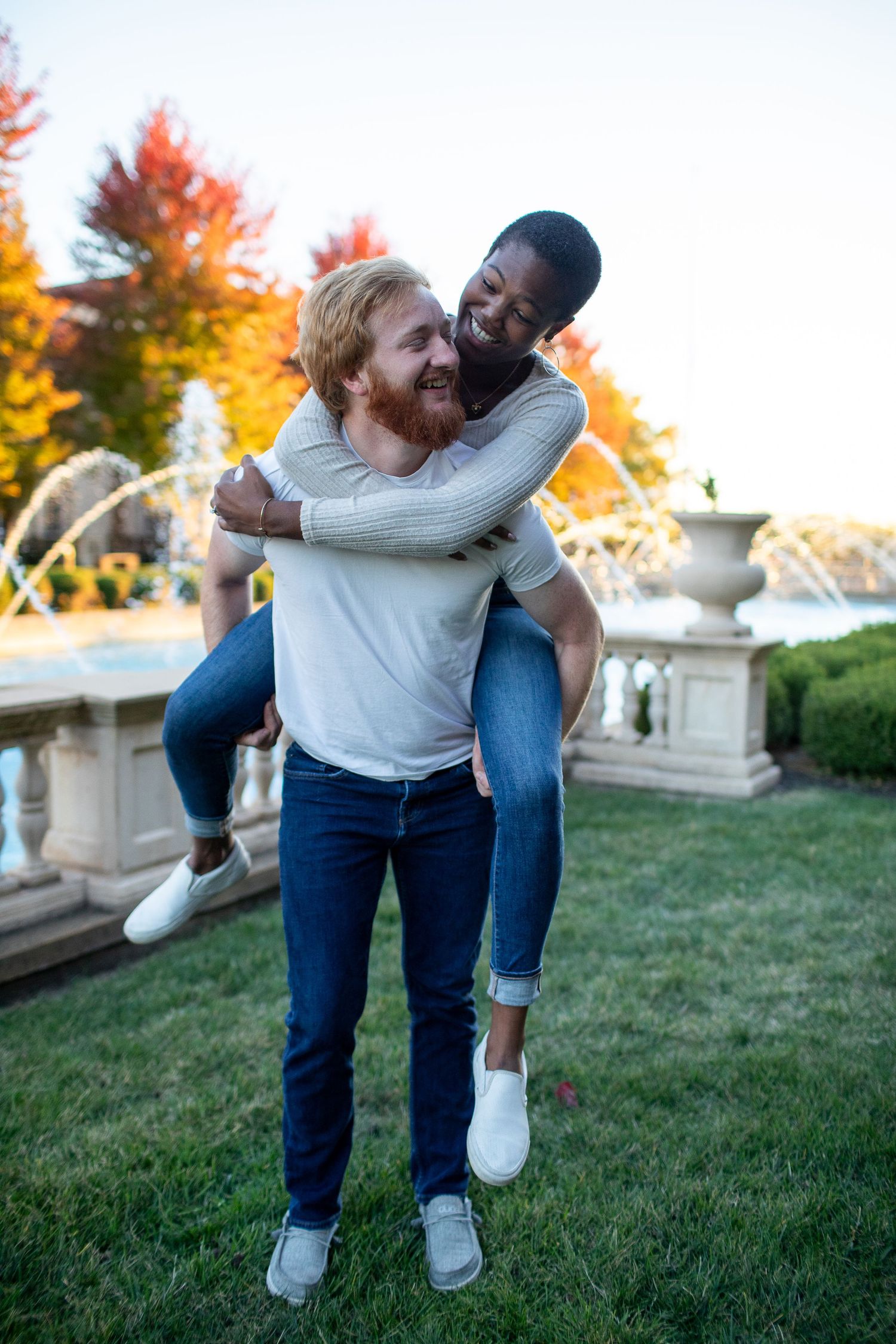 Playful piggyback ride moment between couple on manicured grounds with autumn scenery.