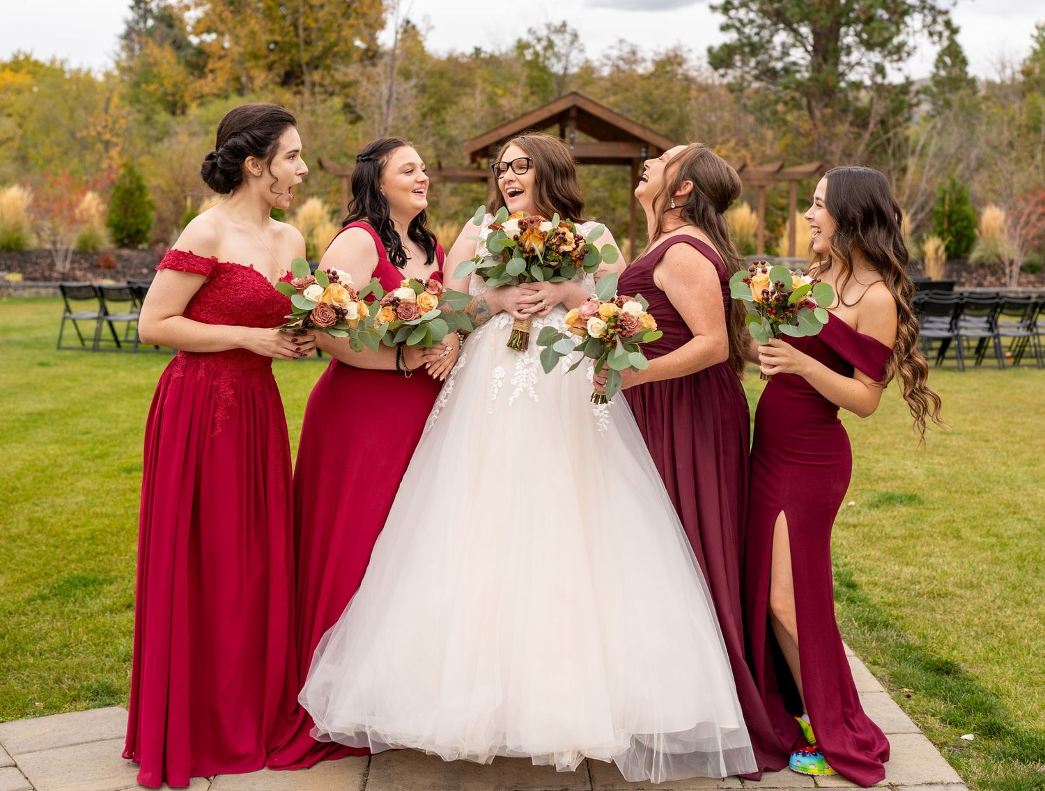 Wedding party in burgundy dresses posing outdoors with autumn foliage in the background.