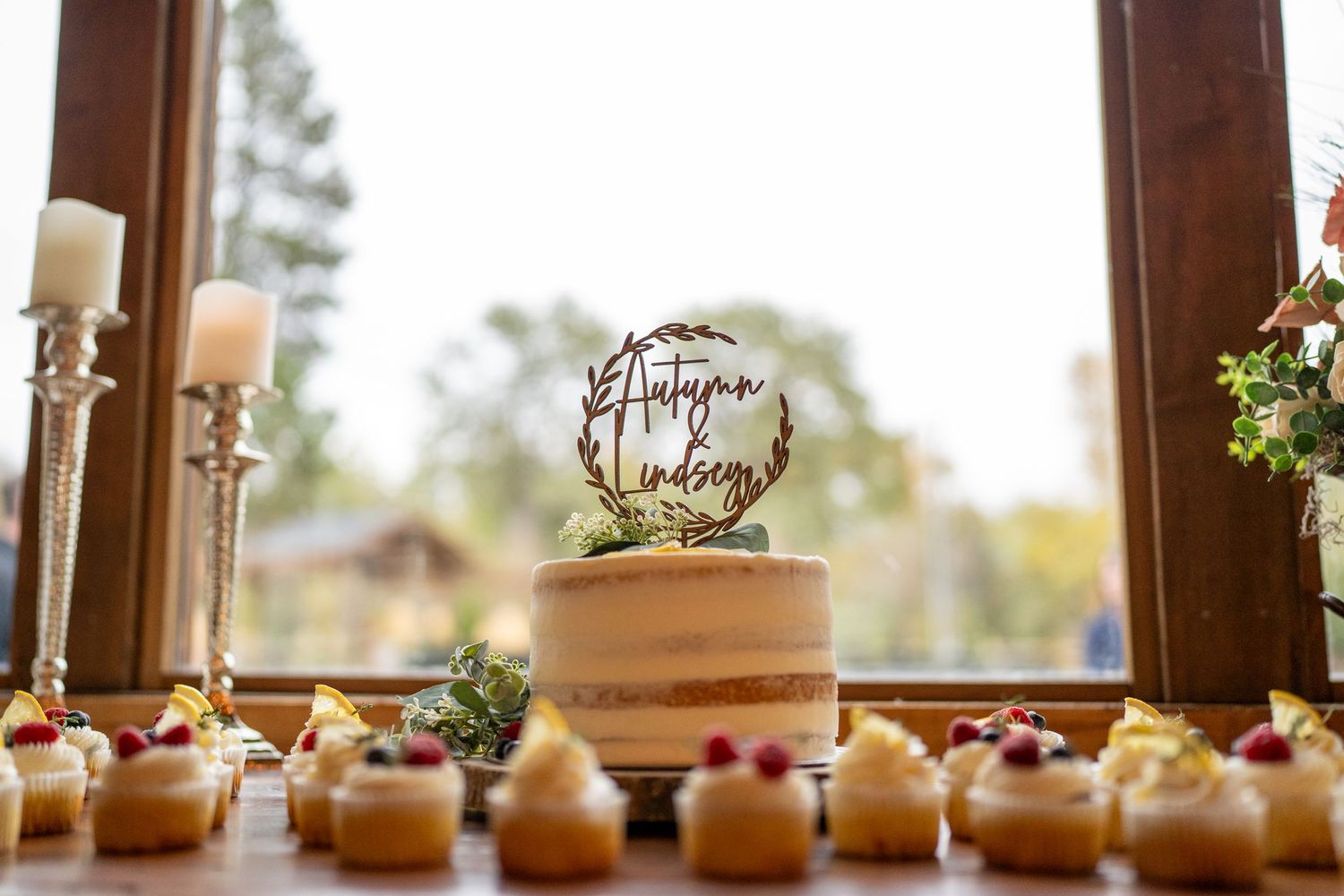Elegant wedding cake and cupcakes displayed on a wooden table with decorative cake topper.