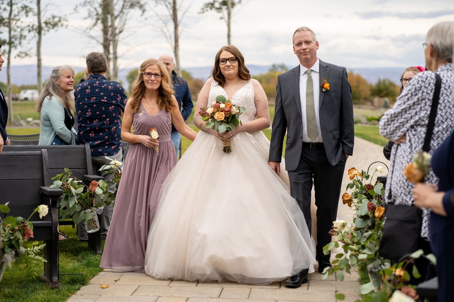 Wedding party walking down outdoor path decorated with floral arrangements.