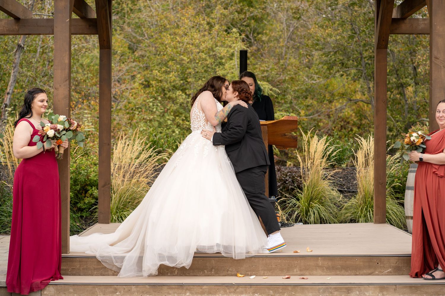 Wedding ceremony moment under a wooden pavilion with attendants in burgundy dresses.