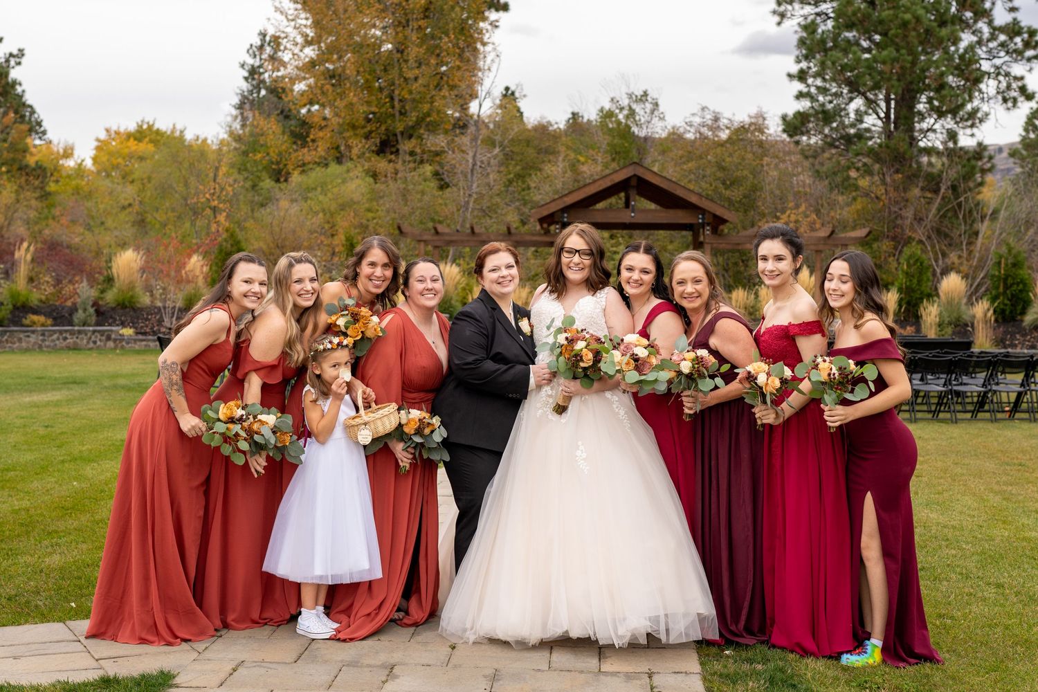 Large wedding party in burgundy dresses gathered for outdoor group photo.