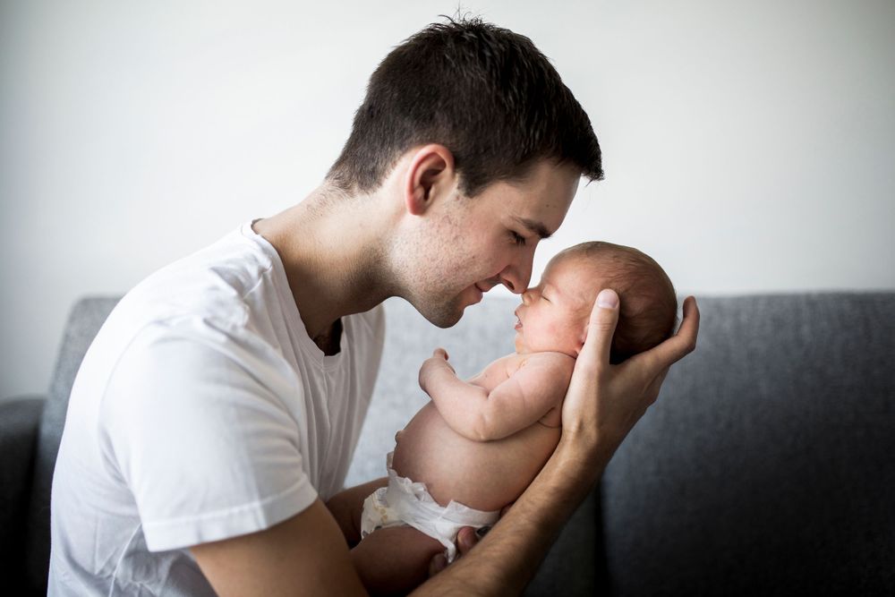 Tender moment between parent and newborn baby on grey couch.