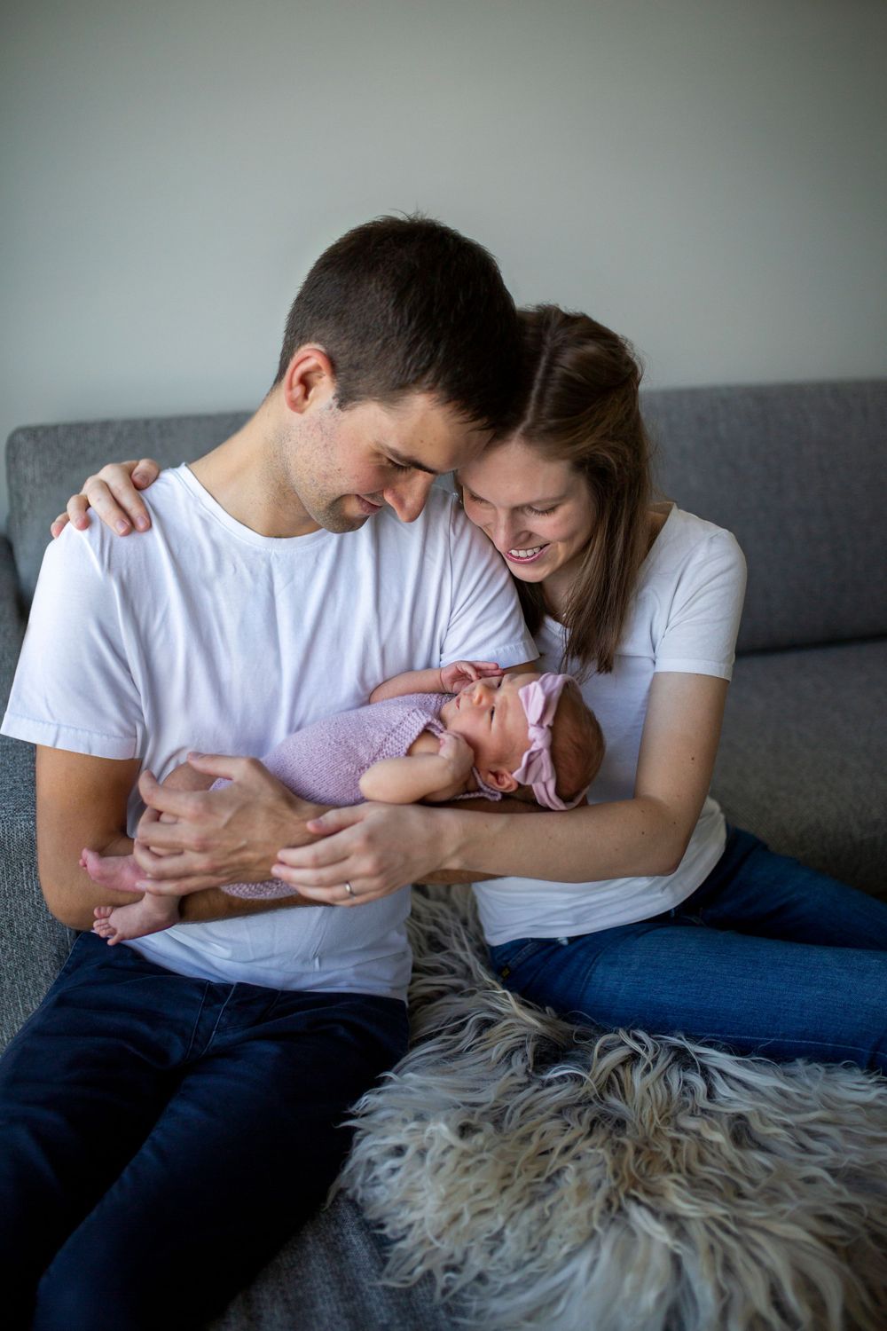Parents share intimate moment with newborn baby on grey couch.