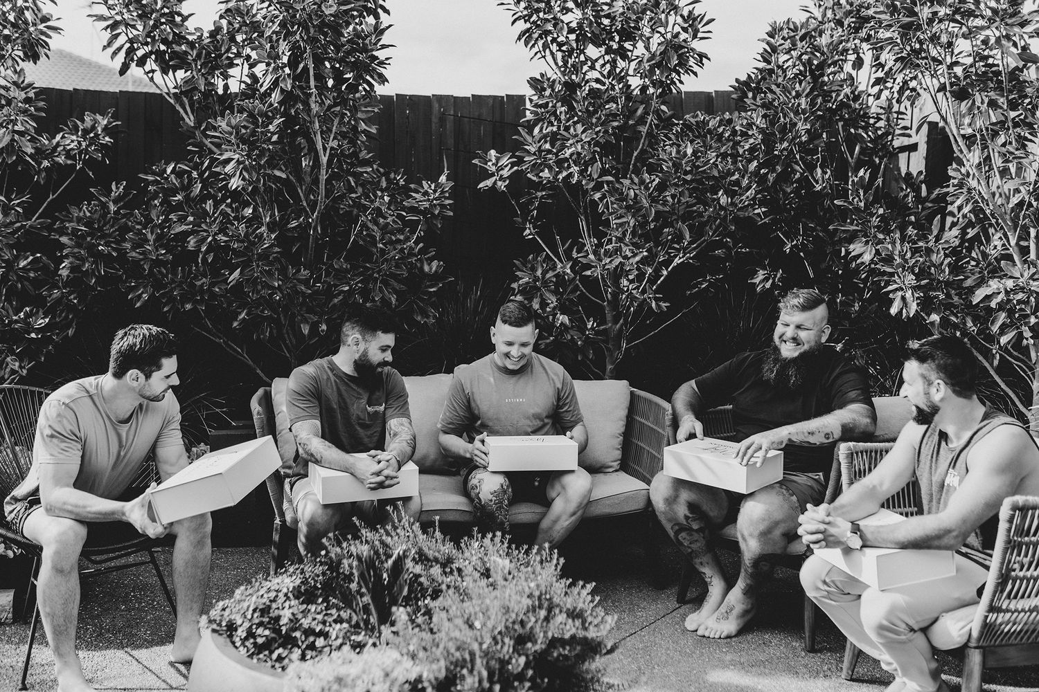 Group sitting outdoors on patio furniture looking at papers together in garden setting.