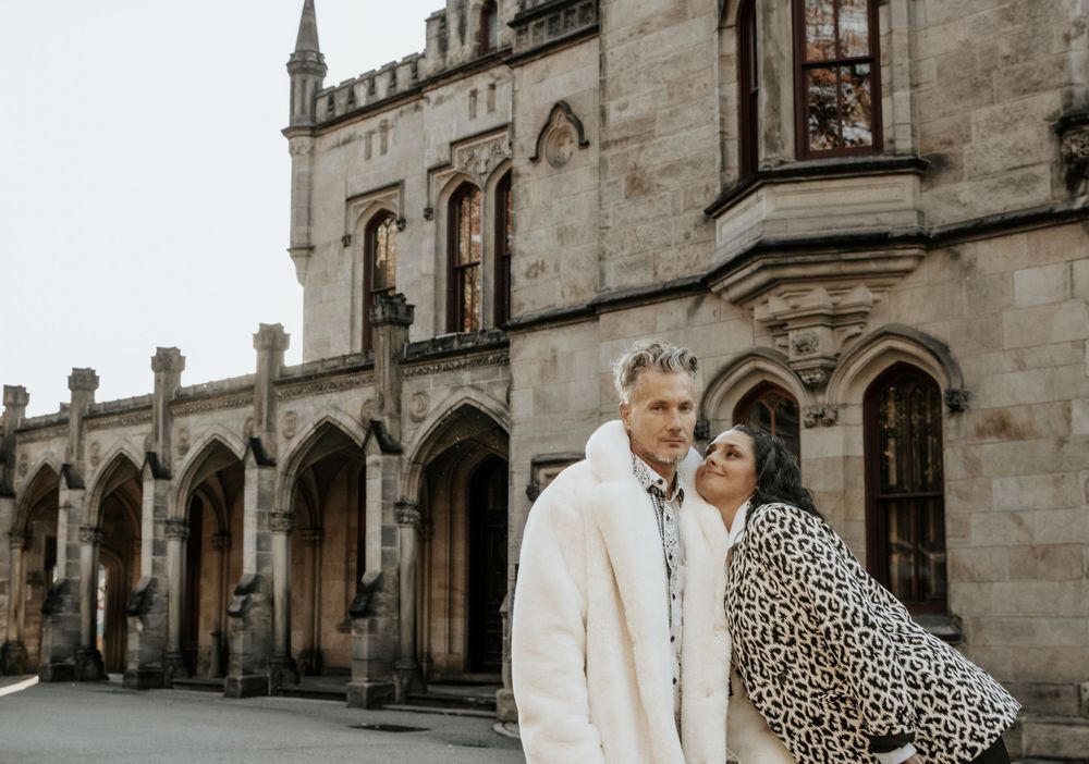 A couple in matching prints poses against Gothic architecture on an overcast day.