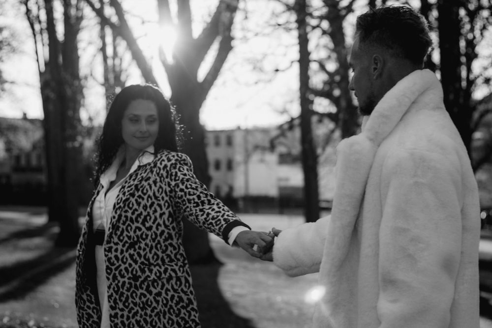 A black and white photo of a couple holding hands in a sunlit park setting.