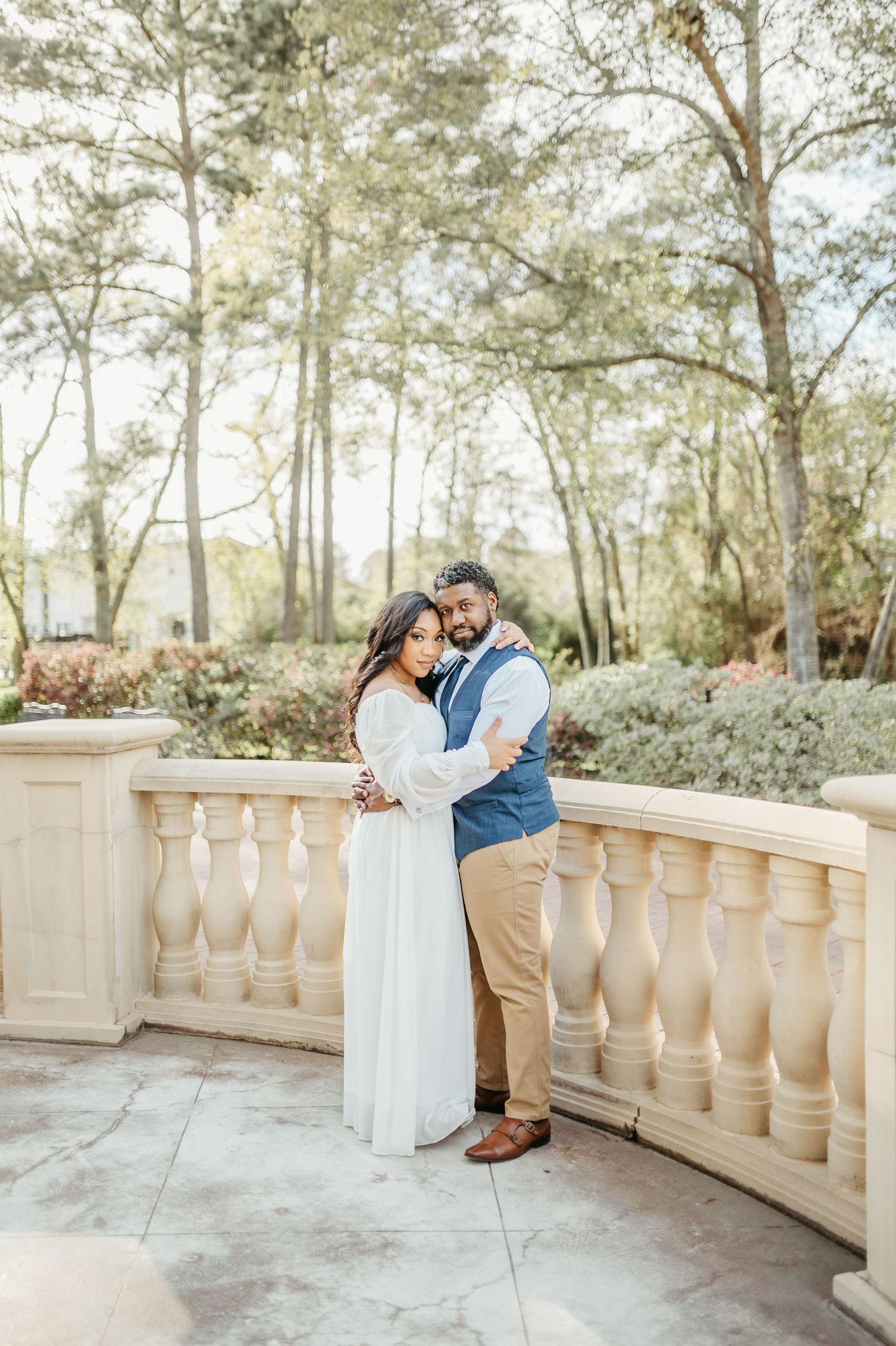 Romantic couple embraces on stone balcony surrounded by sunlit pine trees.