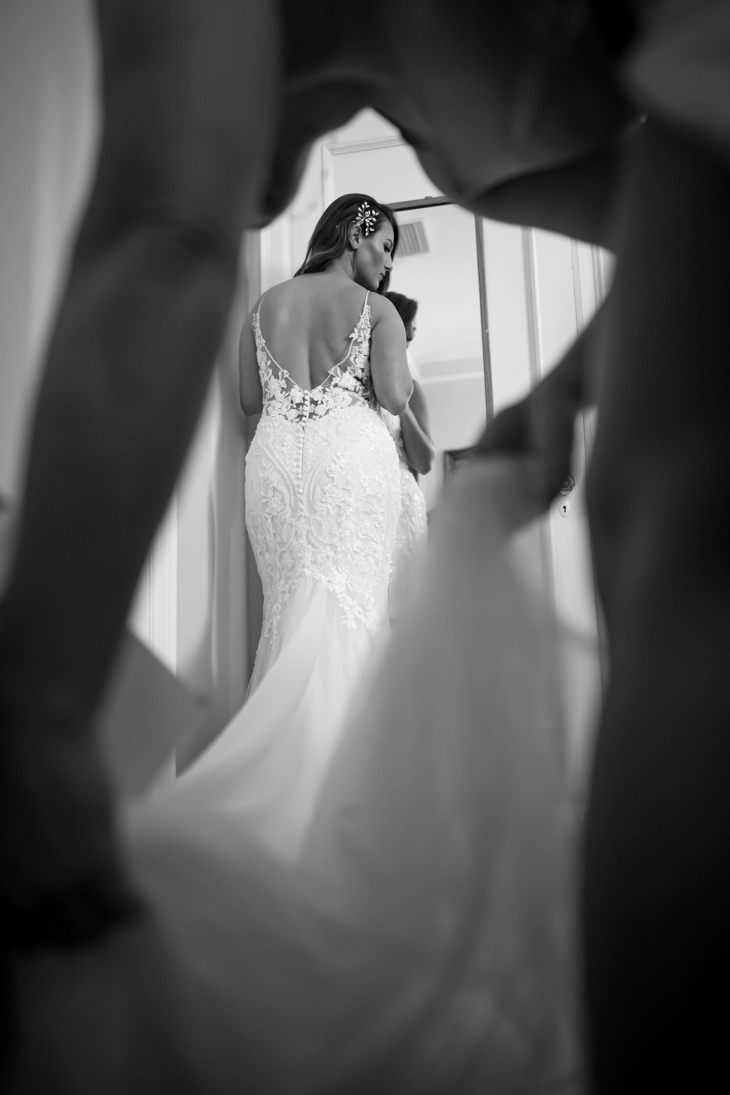 Black and white photo of a bride in a lace back wedding dress framed through silhouettes.