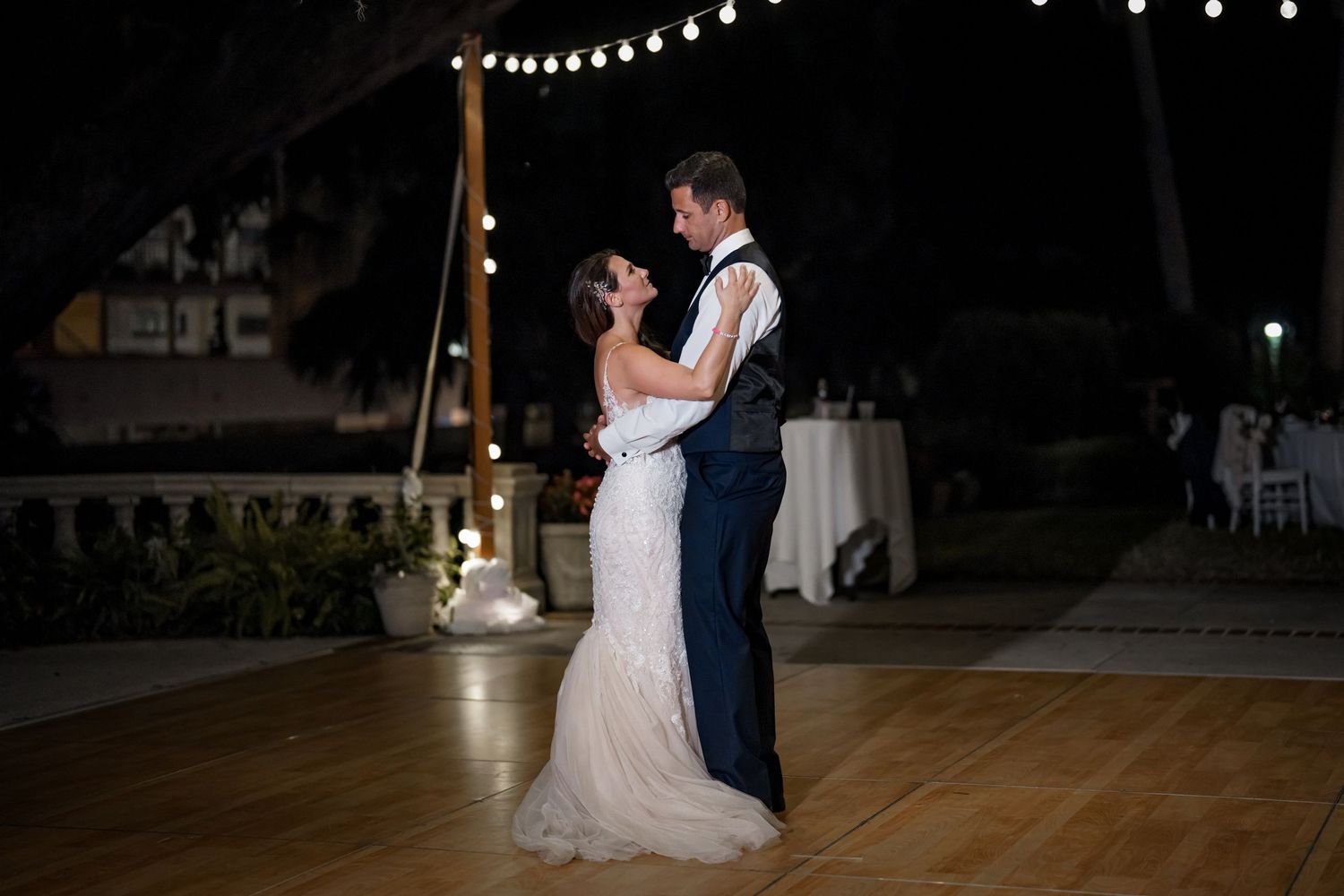 A couple shares an intimate dance moment on a wooden floor under twinkling outdoor lights.