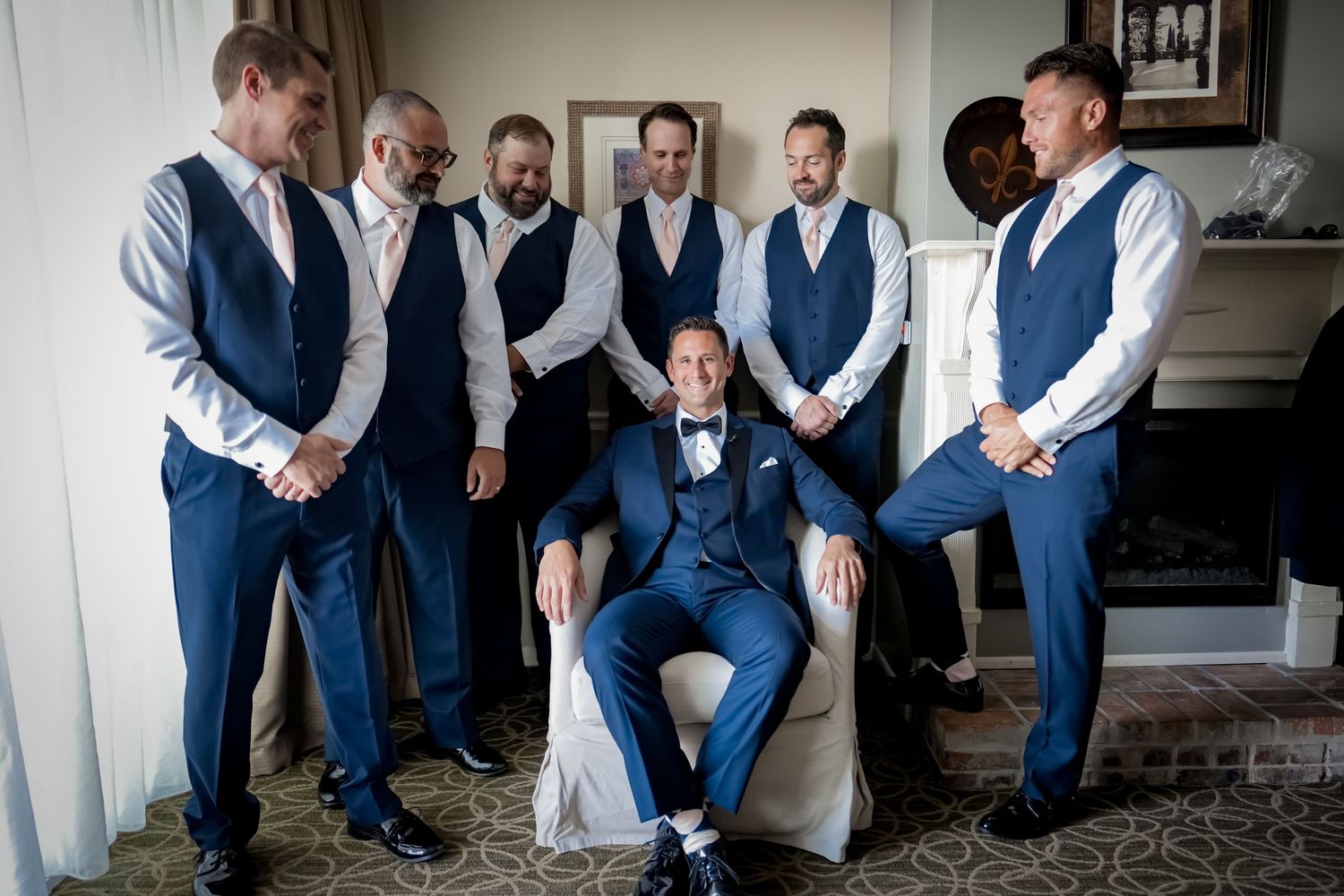 A wedding party in navy blue vests poses together in a formal room setting.