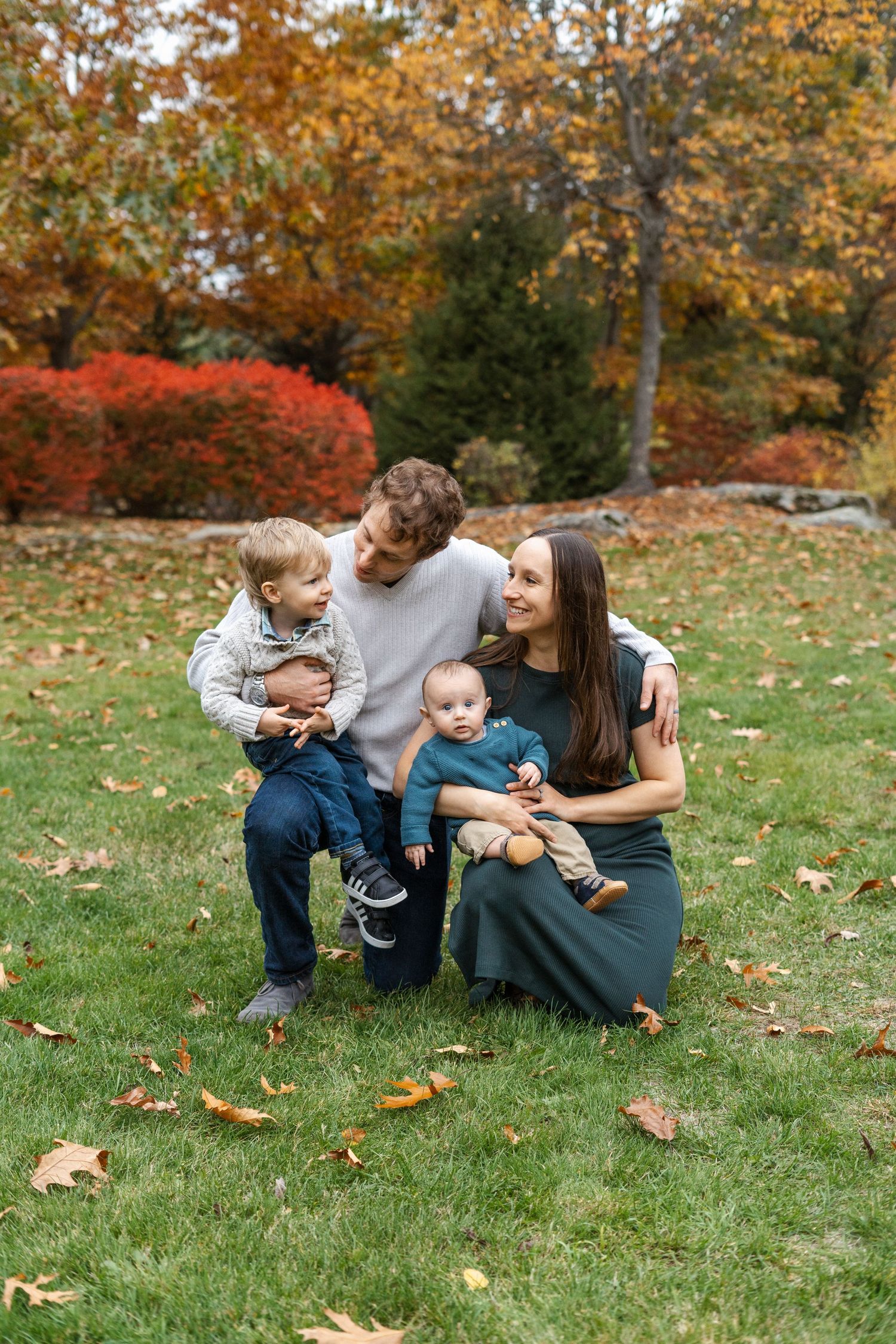 Family sitting on grass during fall season with colorful foliage.