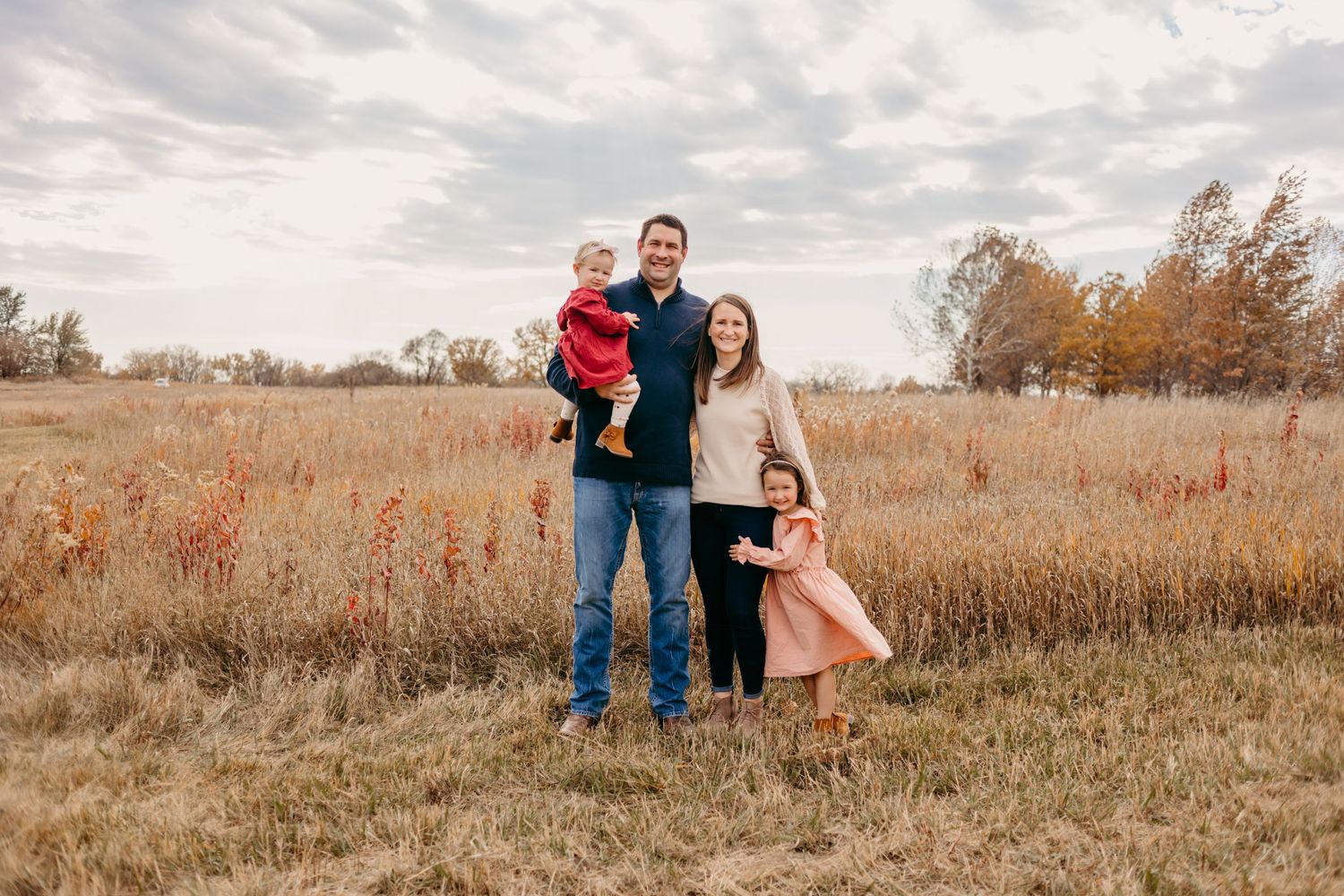 Family poses together in a golden autumn field under cloudy skies.