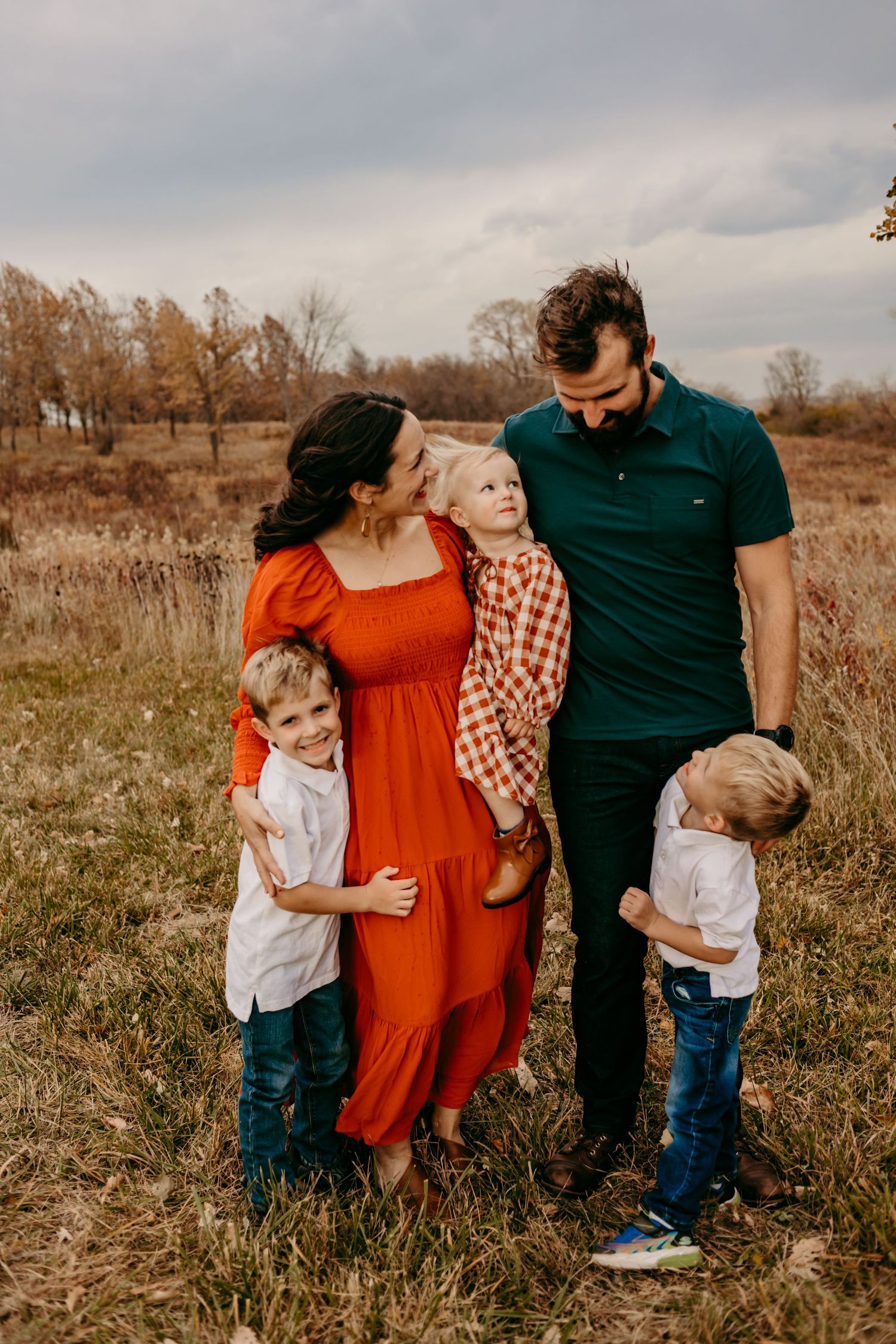 A family of four pose together outdoors in a field during autumn wearing coordinating outfits.