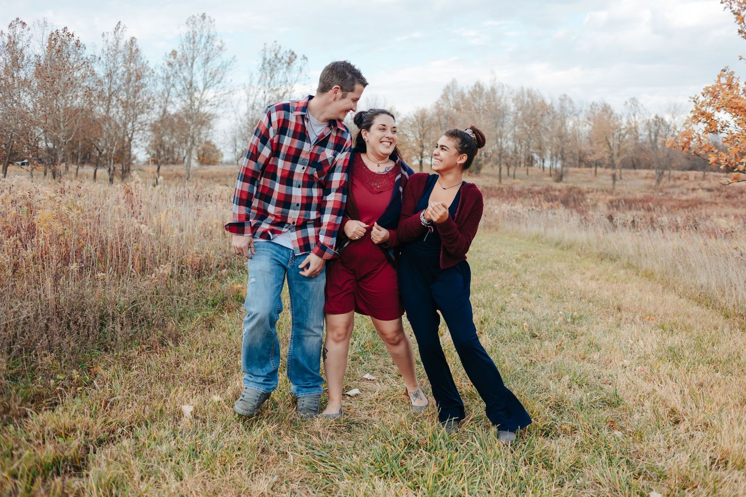 Three people share a playful moment in a fall field with dried grass.
