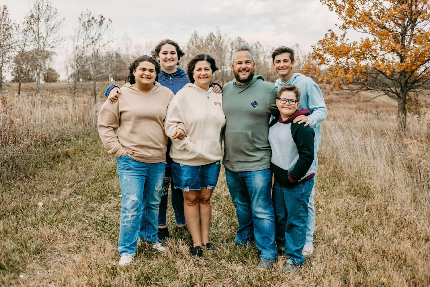 A group poses together in a grassy field during fall with trees in the background.