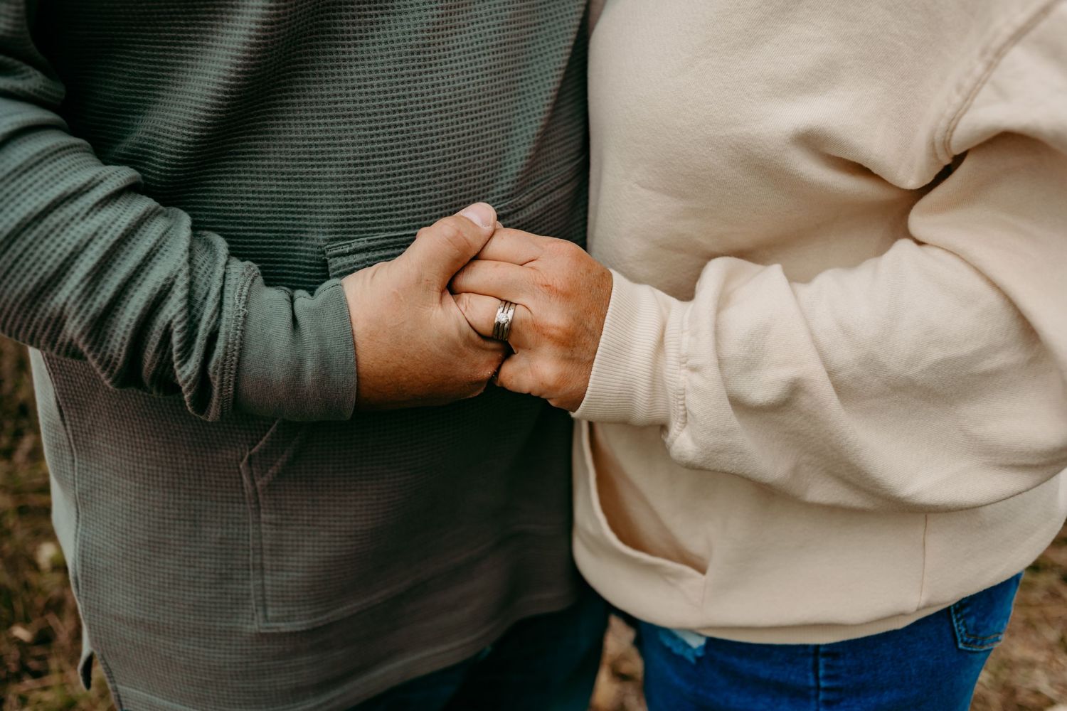Close up view of two people holding hands showing wedding rings against casual clothing.
