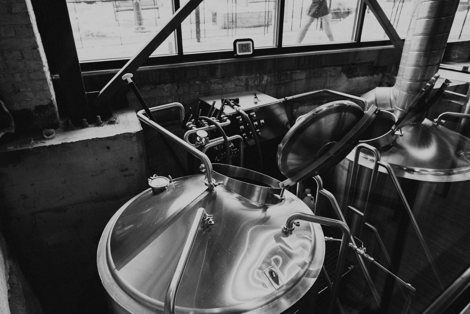 Black and white image of professional brewing equipment with metal tanks and pipes.