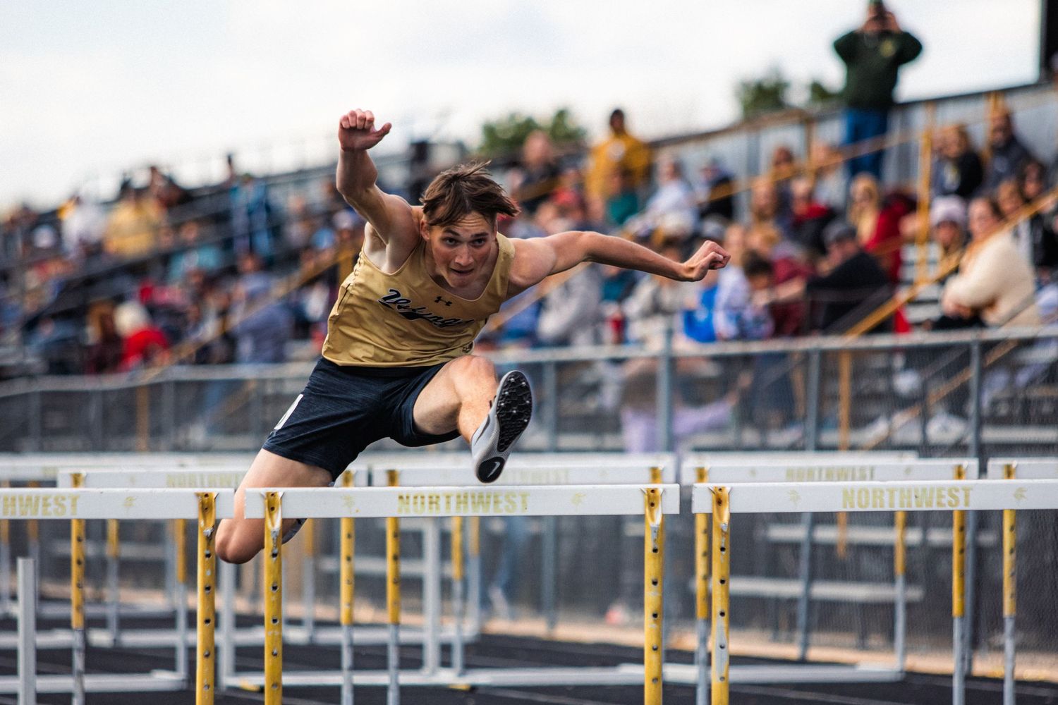 Track athlete clearing hurdles during competitive race at outdoor stadium.