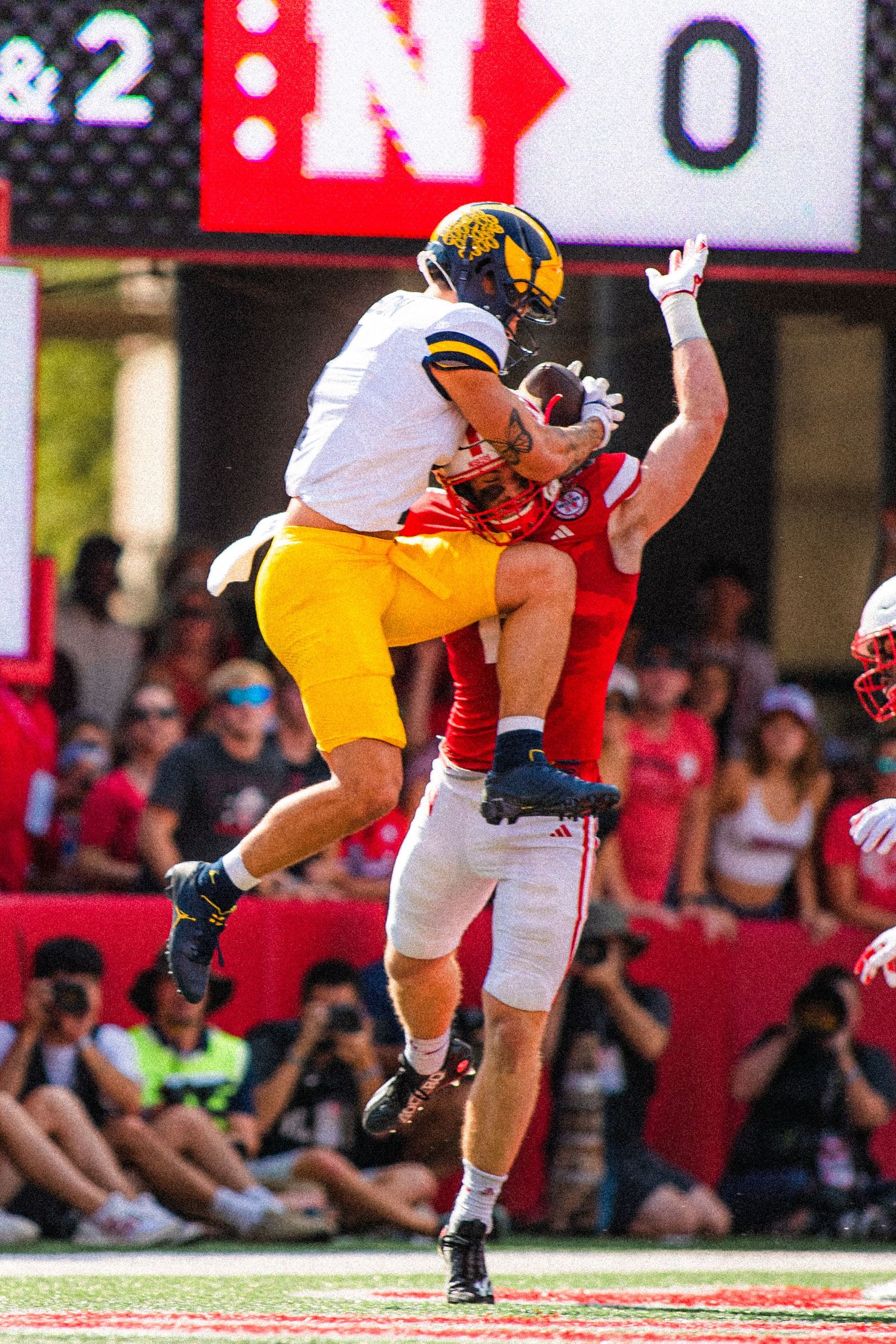 College football players leap high in the air during an intense play between Michigan and Nebraska.