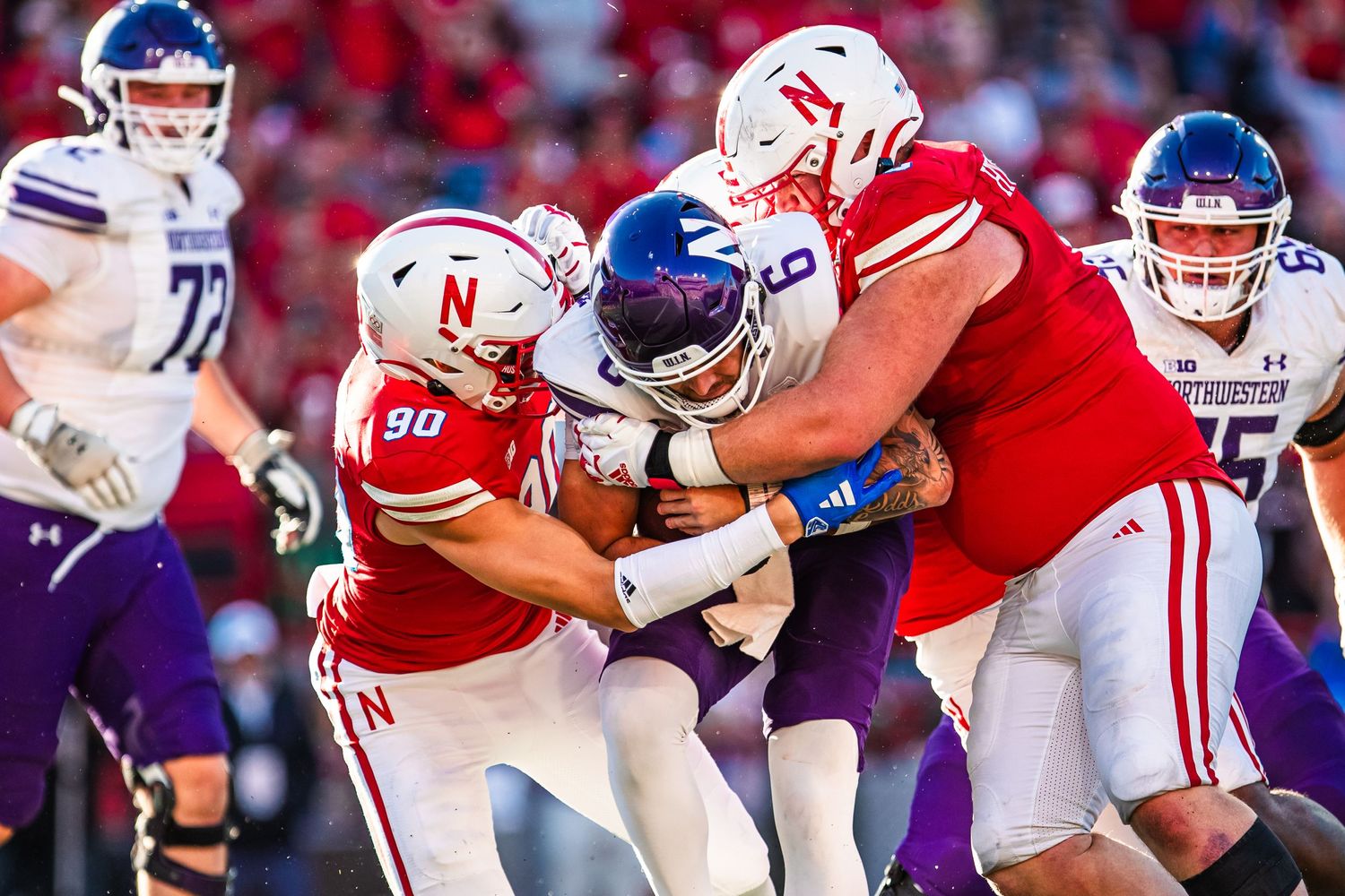 Football players from Nebraska and Kansas State clash in a defensive struggle during a game.
