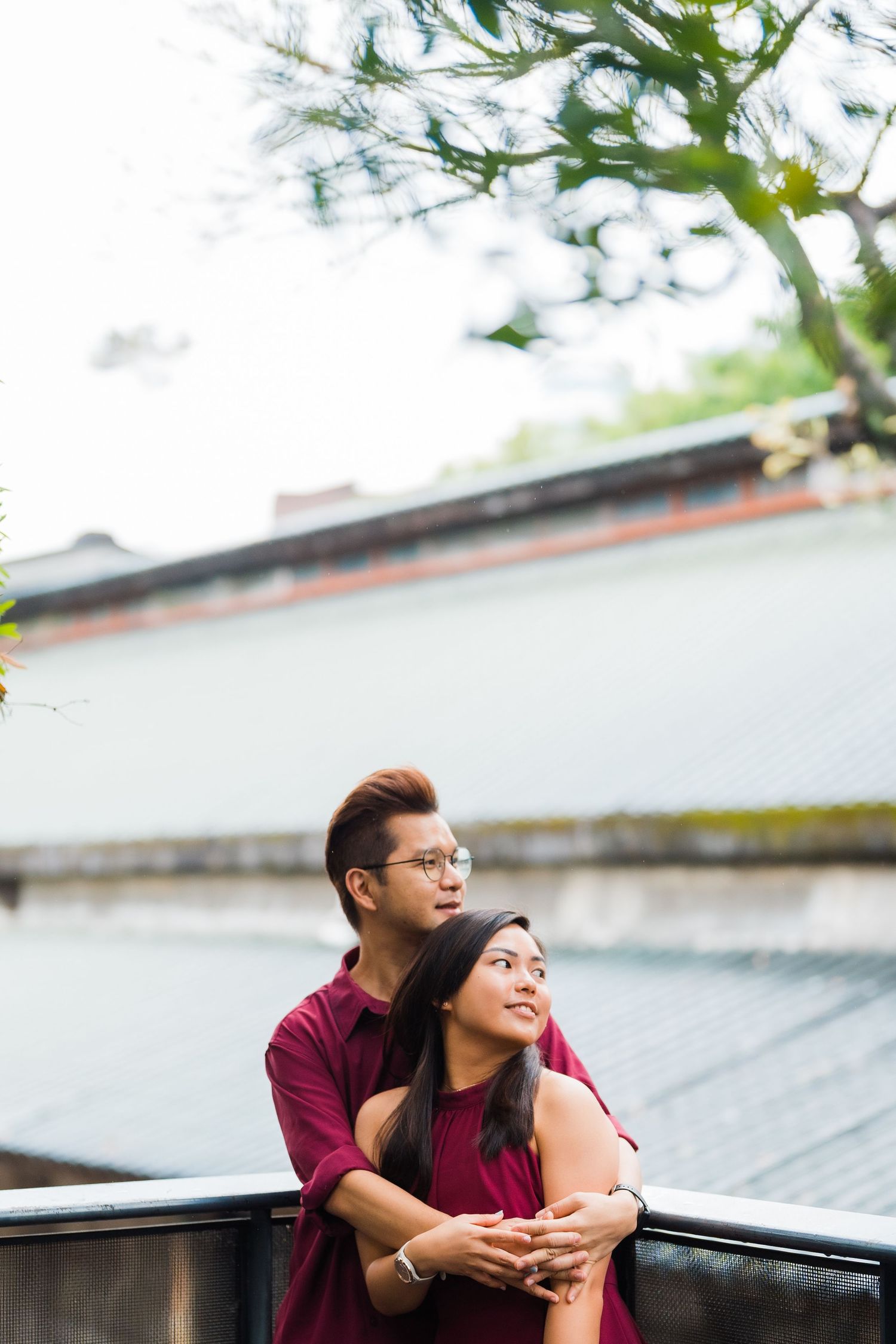 Romantic couple in burgundy outfits embracing by a waterfront railing.
