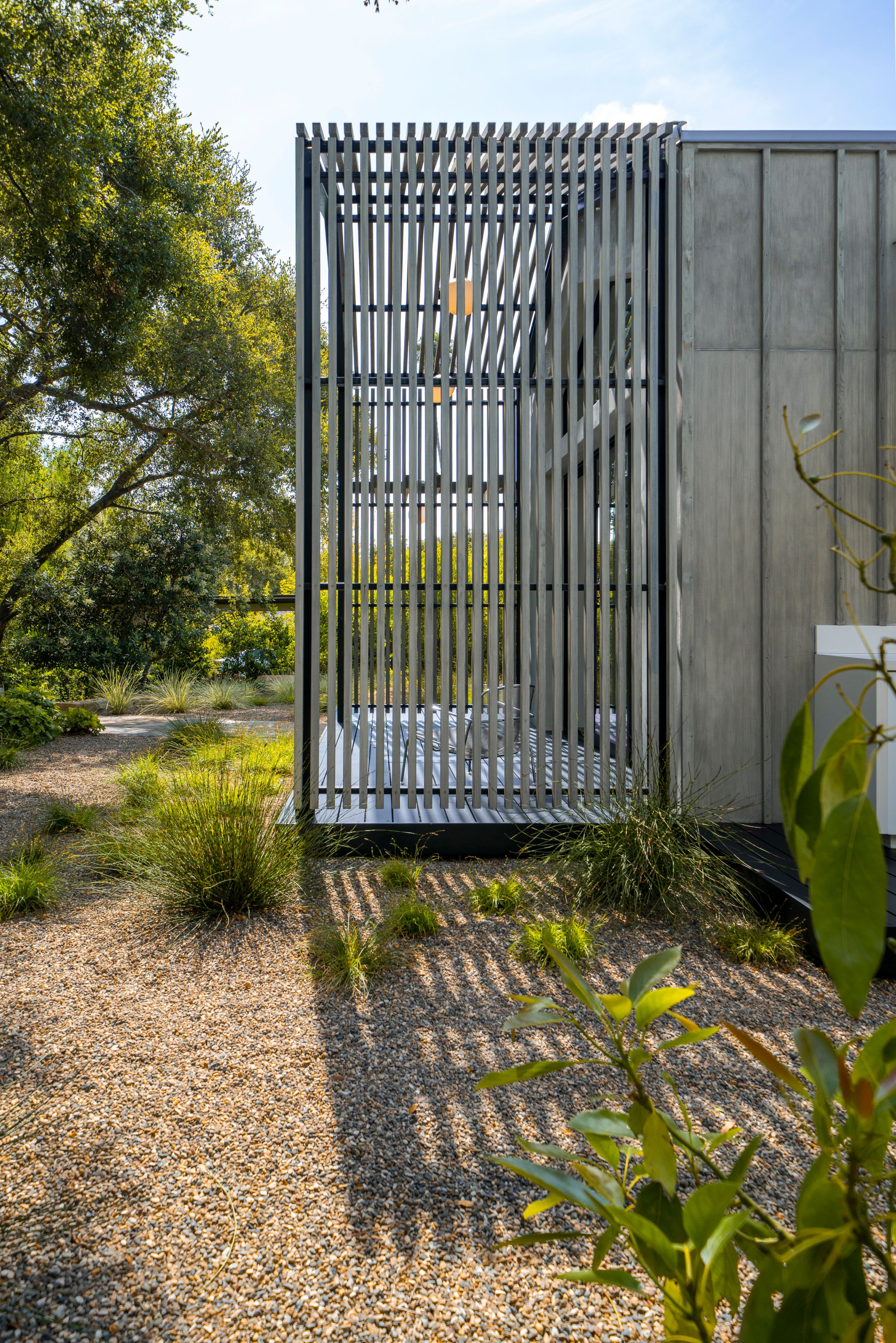 Contemporary building exterior with vertical metal slats creating patterned shadows on gravel path.