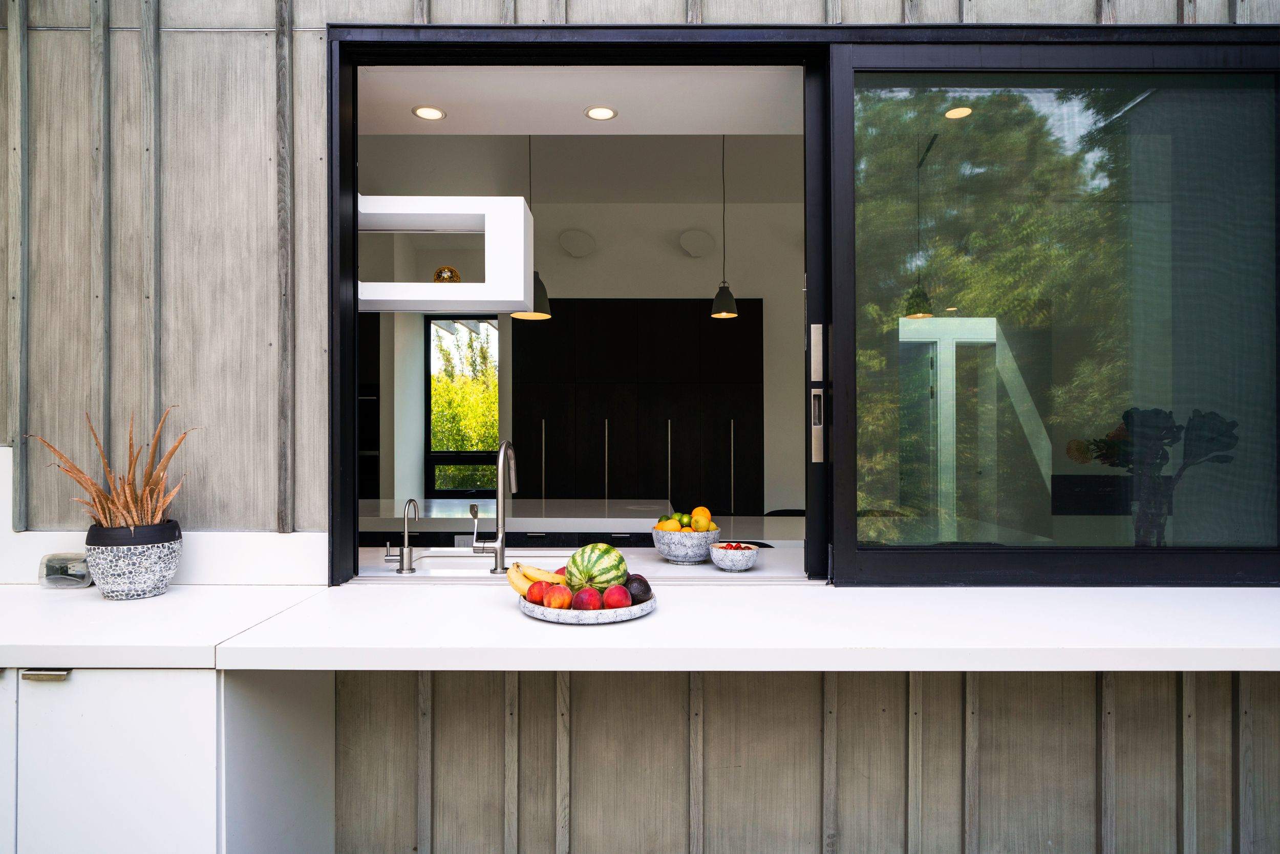 Modern outdoor serving window with white counter displaying fresh fruit and vegetables.