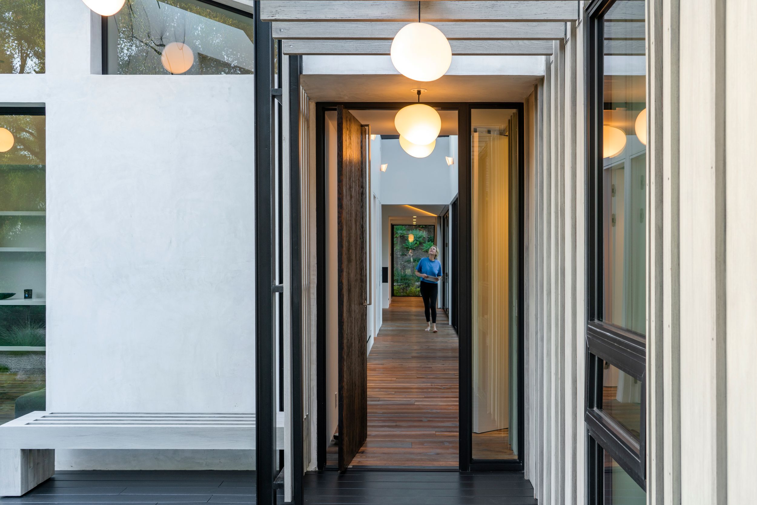 Modern hallway with wooden floors and pendant lighting leading to a bright interior space.
