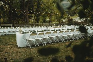 Rows of white folding chairs set up outdoors with string lights and trees in the background for an outdoor event.