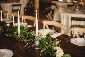 Rustic wedding table decorated with greenery garland, white candles, and elegant place settings.