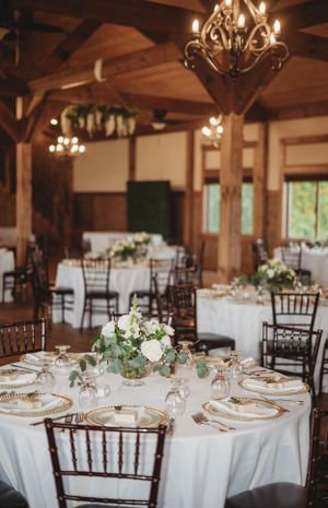 Elegant wedding reception hall with round tables, white linens, and wooden beam ceiling details.