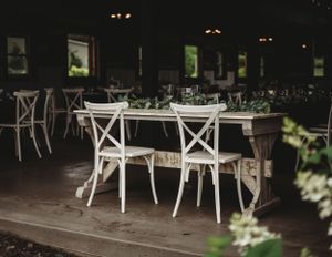 Outdoor dining area with white chairs and tables set up for an evening wedding reception.