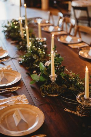Candlelit wedding table setting with fresh greenery garland and gold-rimmed white plates.