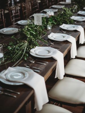 Formal place settings with white napkins and greenery garland on dark wooden tables.
