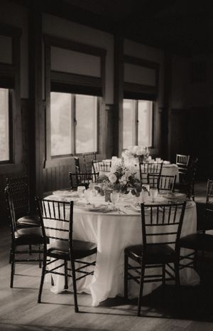 Black and white photo of an empty wedding reception space with round tables and chiavari chairs.