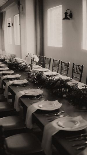 Black and white photo of formal table settings with floral garland runners and wall sconces.