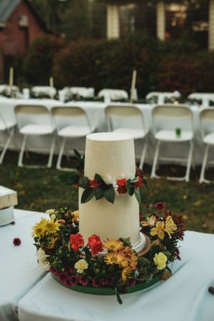 White wedding cake decorated with a floral wreath centerpiece featuring red and yellow blooms.