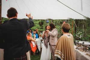 Wedding guests gather outdoors under a white tent for a celebration.