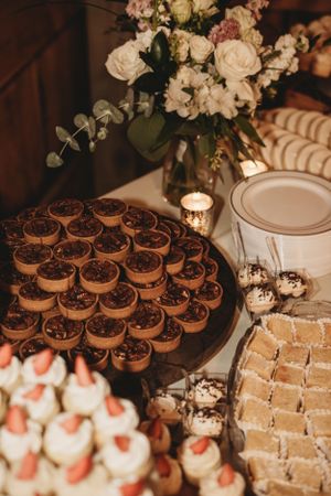 Wedding dessert display featuring chocolate tarts and strawberry-topped mini cakes on white plates.
