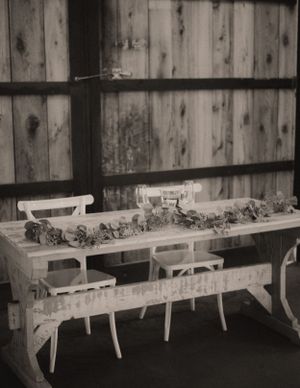 Long wooden benches with white cushions arranged against a rustic barn wall for wedding seating.