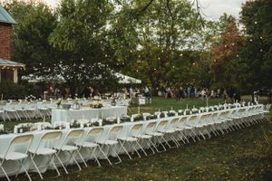 Long rows of white folding chairs and tables set up on a lawn near a brick building for an outdoor reception.