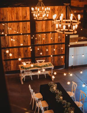 Rustic barn wedding venue with warm lighting, wooden beams, and white chairs arranged for a ceremony.