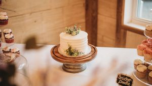 Simple white wedding cake displayed on a wooden cake stand with greenery accents.
