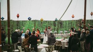 Wide angle view of wedding reception setup with hanging lanterns and forest backdrop.
