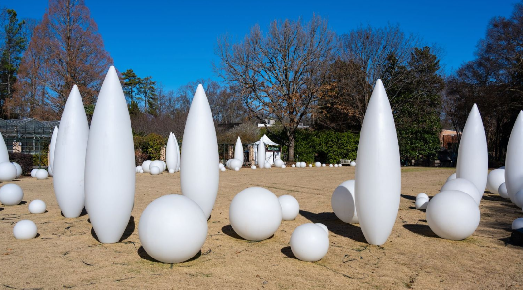 Installation art featuring white egg-shaped sculptures arranged on sandy ground.