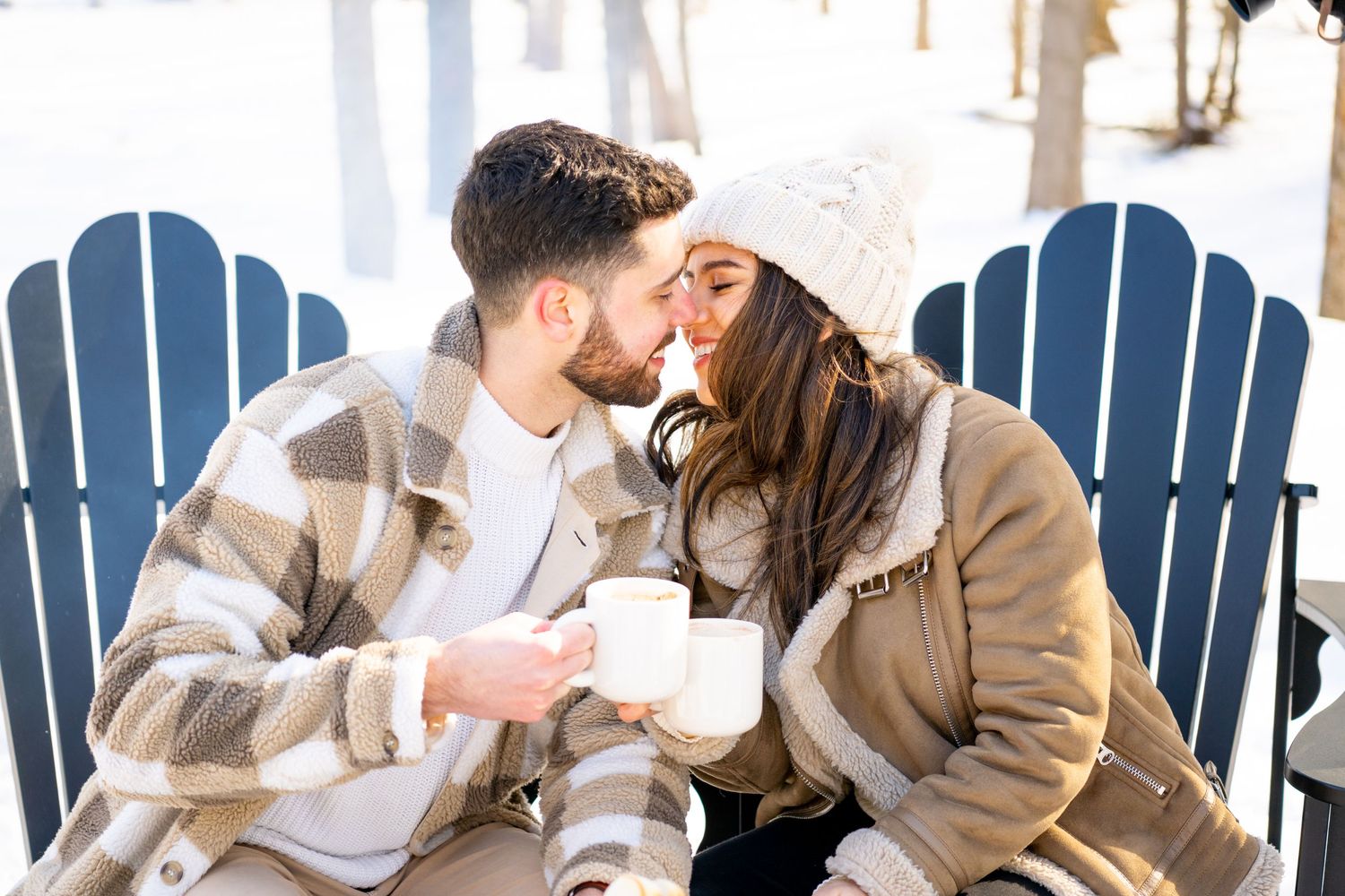 A cozy winter scene with a couple sharing a moment on blue Adirondack chairs.