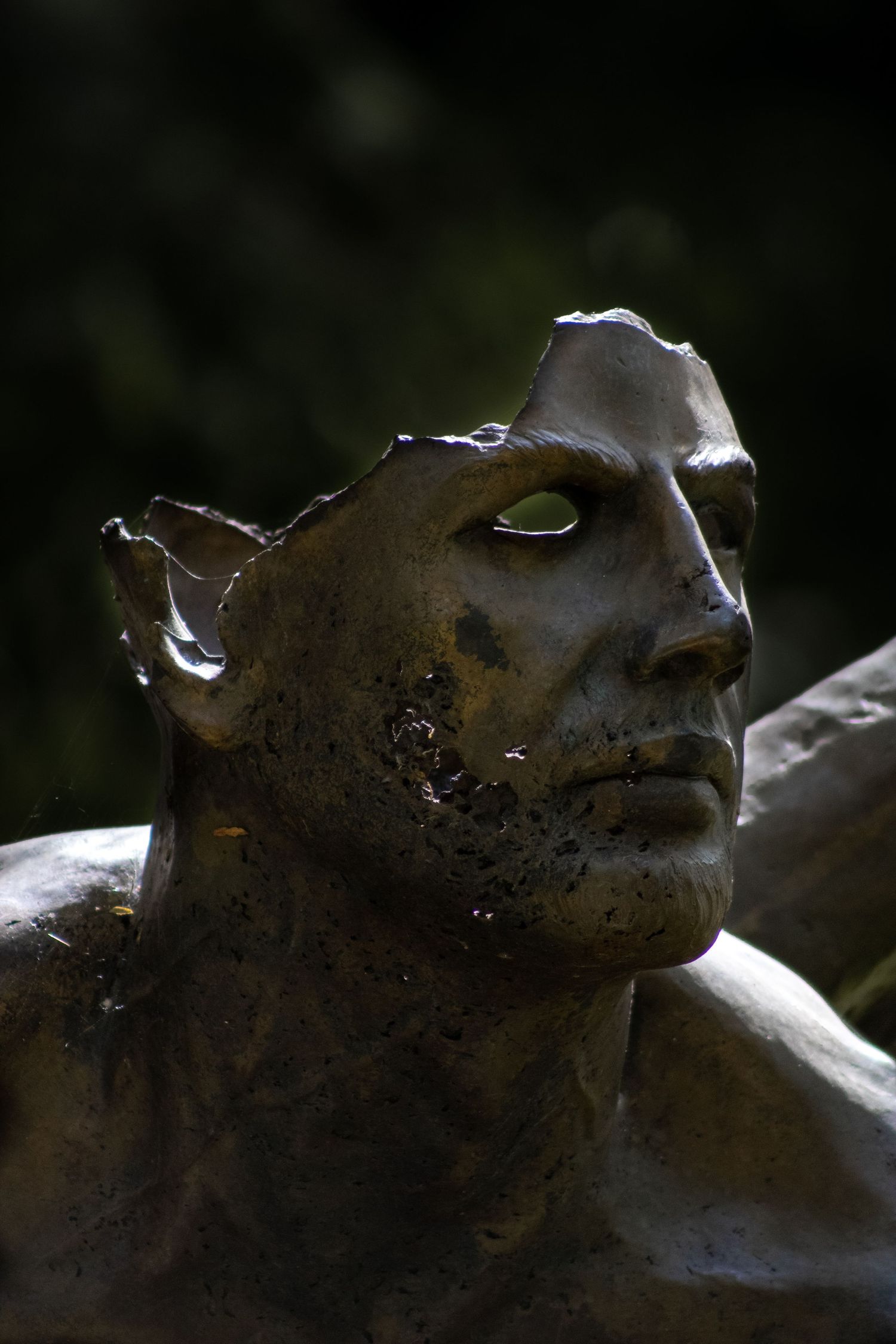 Dark bronze sculpture of a mythical elf-like figure with pointed ears in dramatic lighting.