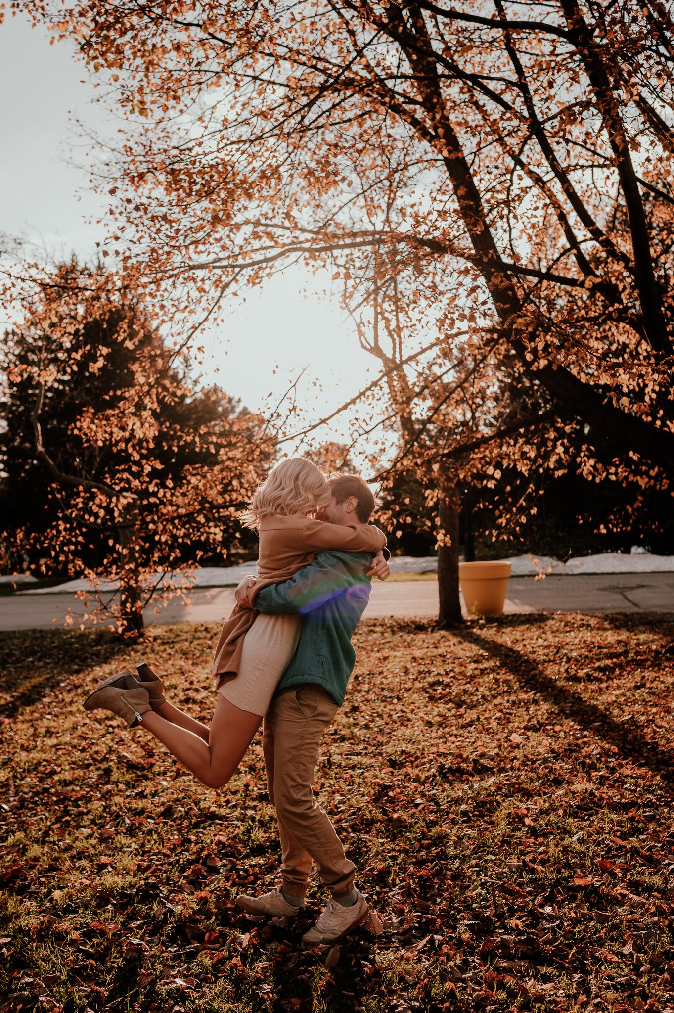 Joyful embrace between couple under autumn trees with golden sunlight filtering through.