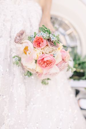 A delicate bridal bouquet with pink garden roses and white flowers against a lace dress background.